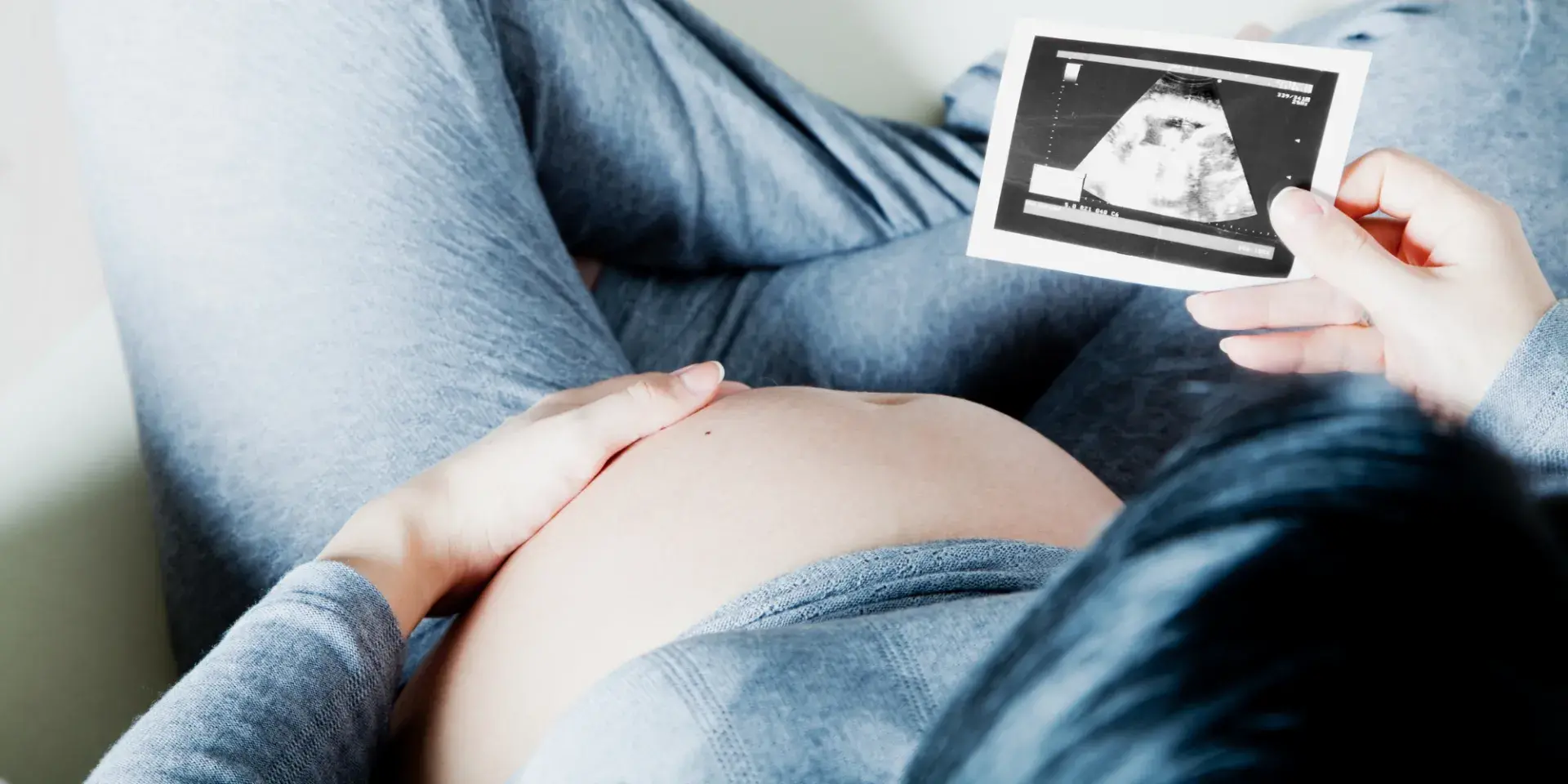 Woman in grey tracksuit cradles baby bump holding ultrasound scan