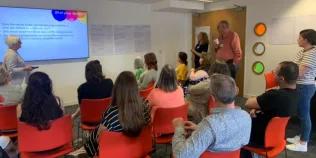 An image taken from the back of room, with people sitting in seats facing a screen at the front.