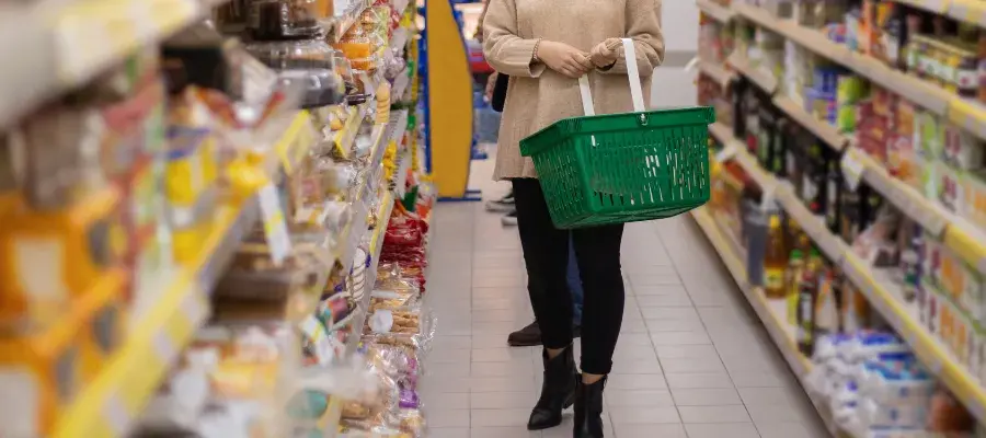 Woman walking down supermarket aisle with green basket