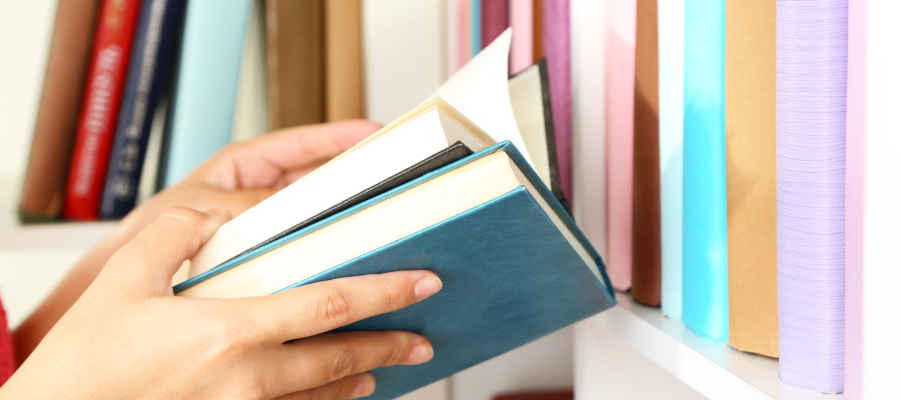 Close up of hands holding two books with book shelf in background