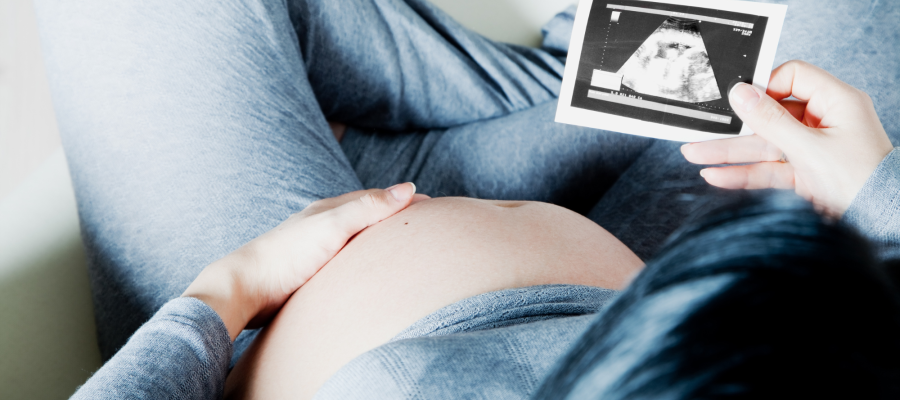 Woman in grey tracksuit cradles baby bump holding ultrasound scan
