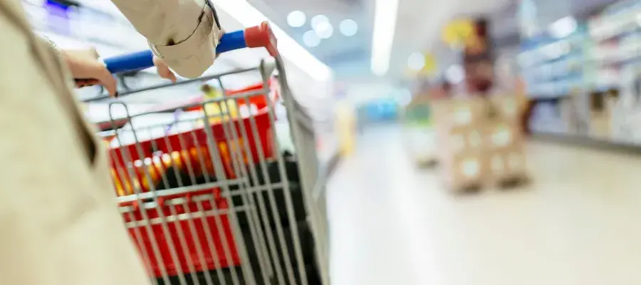 Close up of person pushing shopping trolley down supermarket aisle