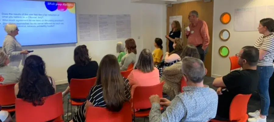 An image taken from the back of room, with people sitting in seats facing a screen at the front.