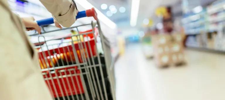 Close up of person pushing shopping trolley down supermarket aisle